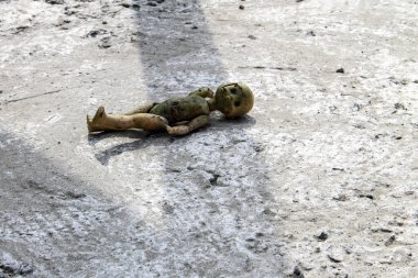 Gri beton zeminde terk edilmiş kırık bir oyuncak bebek.