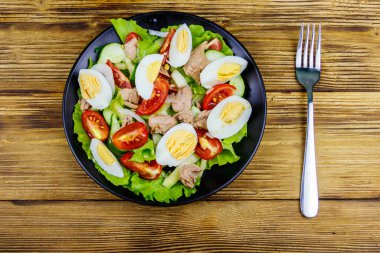 Yumurtalı lezzetli ton balığı salatası, marul ve ahşap masada taze sebze. Üst görünüm