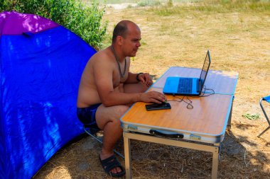 Piknik masasında dizüstü bilgisayarını kullanan bir adam. Seyahat ederken çalışmak. Serbest bir iş. İş ve seyahat kavramı