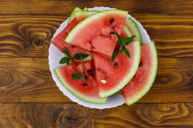 Tahta bir masanın üzerinde beyaz tabakta taze olgun dilimlenmiş karpuz. Üst görünüm