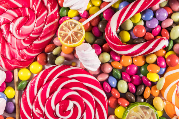 Background of colorful chocolate candies, lollipops, candy cane and marshmallows