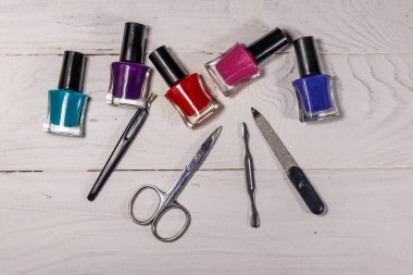 Beyaz ahşap arka planda temel manikür aletleri seti. Tırnak makası, tırnak makası, tırnak törpüsü ve oje şişeleri.