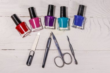Beyaz ahşap arka planda temel manikür aletleri seti. Tırnak makası, tırnak makası, tırnak törpüsü ve oje şişeleri.