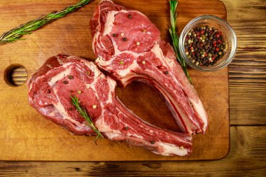 Kemiğin üzerinde çiğ biftek, baharatlar ve ahşap masada biberiye. Üst görünüm