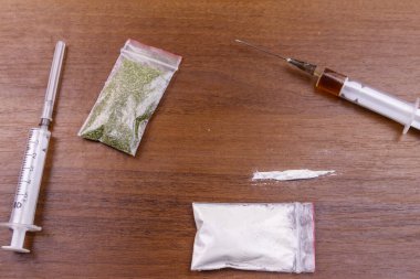 Farklı tipte uyuşturucular: Kokain, eroin şırıngası ve masada kurutulmuş kenevir. Uyuşturucu kullanımı, suç ve bağımlılık kavramı