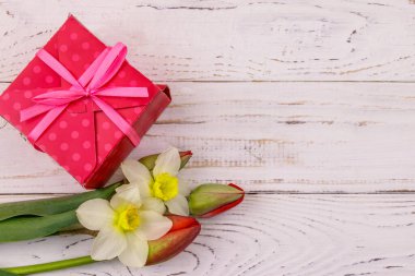 Hediye kutusu ve beyaz ahşap arka planda kırmızı laleler ve nergisler. Sevgililer Günü, Kadınlar Günü, Anneler Günü ve Doğum Günü kavramı. Üst görünüm, alanı kopyala