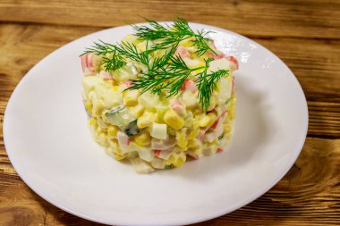 Yengeç çubuklu salata, tatlı mısır, salatalık, yumurta ve mayonez ahşap masada.