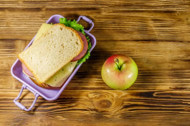 Tahta bir masanın üzerinde sandviç ve elma olan beslenme çantası. Üst görünüm