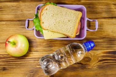 Sandviçli beslenme çantası, ahşap bir masada bir şişe su ve elma. Üst görünüm