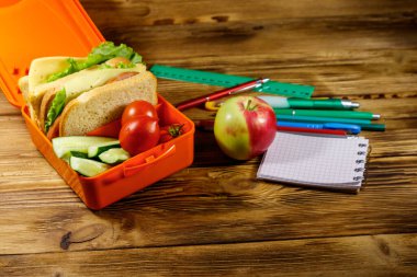 Okul konseptine geri dönelim. Okul malzemeleri, elma ve beslenme çantası, sandviçler ve taze sebzeler ahşap bir masada.