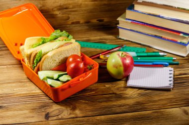 Okul konseptine geri dönelim. Okul malzemeleri, kitaplar, elma ve beslenme çantası içinde sandviçler ve ahşap bir masada taze sebzeler.