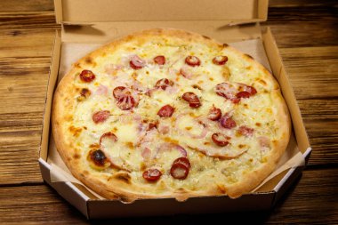 Tahta bir masanın üzerindeki karton kutuda nefis taze pizza. Yemek teslimatı, fast food, pizza teslimatı.