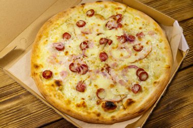 Tahta bir masanın üzerindeki karton kutuda nefis taze pizza. Yemek teslimatı, fast food, pizza teslimatı.