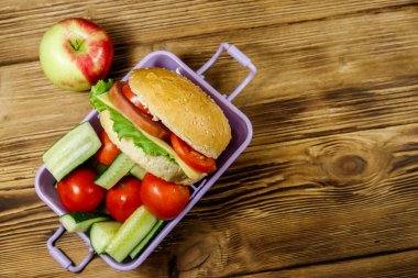 Elma, hamburger ve ahşap masada taze sebzeli beslenme çantası. Üst görünüm