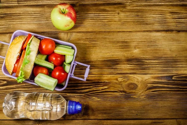 Bir şişe su, elma ve beslenme çantası, içinde hamburgerler ve ahşap bir masada taze sebzeler. Üst görünüm, alanı kopyala