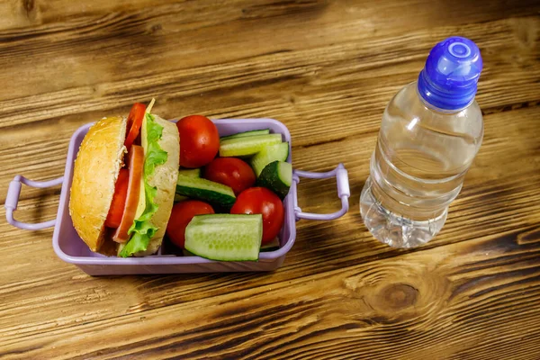 Bir şişe su, hamburgerler ve taze sebzeler ahşap bir masada.