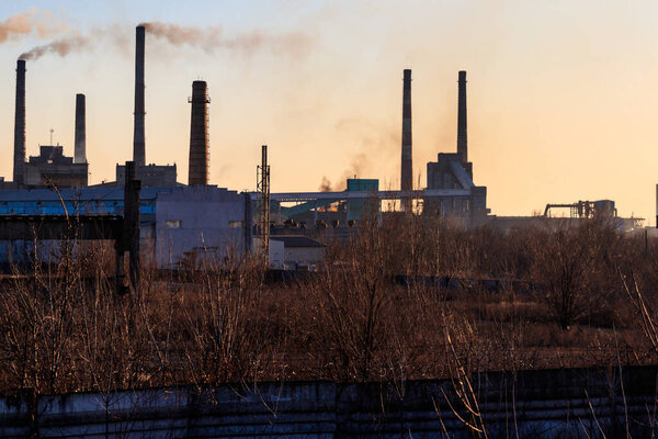 Вид на старый завод с трубами с дымом. Загрязнение воздуха, экологический ущерб