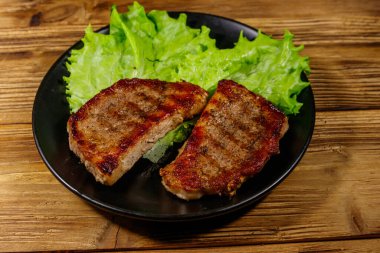 Ahşap masada marul yapraklı ızgara domuz bifteği.