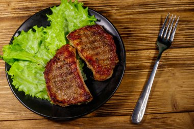 Ahşap masada marul yapraklı ızgara domuz bifteği. Üst görünüm