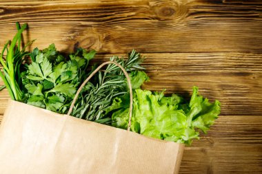 Yeşil soğanlı kağıt torbası, biberiye, marul yaprakları ve ahşap masada maydanoz. Üst Manzara. Sağlıklı gıda ve market alışverişi kavramı