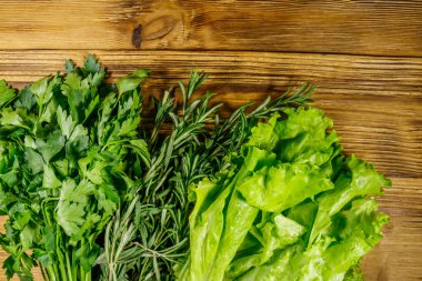 Taze yeşil maydanoz, marul yaprakları ve ahşap masada biberiye otları. Üst görünüm