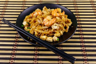 Tayland usulü kızarmış pirinç eriştesi, karides ve bambu hasırında soya peyniri. Tayland yemeği.