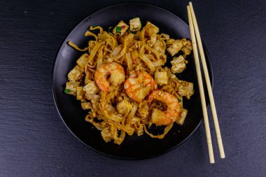 Kızarmış pirinç eriştesi, karidesli Pad Thai ve siyah arkaplanlı bir tabakta tofu. Üst Manzara. Tayland yemeği.