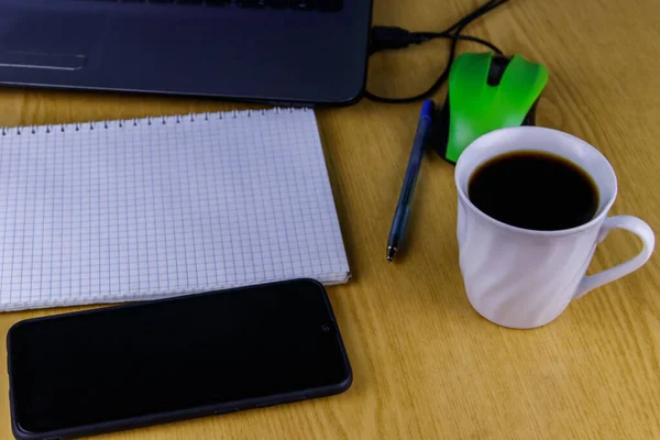 Laptop with mouse, smartphone, notebook, pen and cup of coffee on a desk. Working at home and business concept