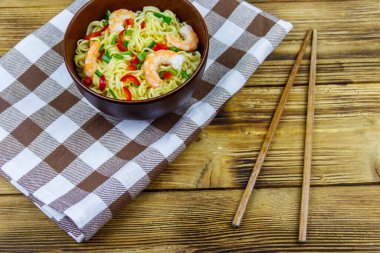 Bir kase karidesli Çin eriştesi, yeşil soğan ve ahşap masada kırmızı acı biber.