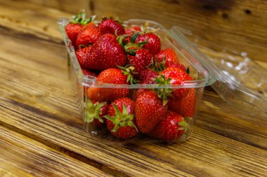 Tahta bir masada plastik kutuda taze çilek.