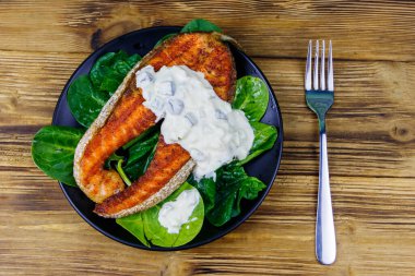 Ahşap masada ıspanaklı ve tartar soslu ızgara somon bifteği. Üst görünüm