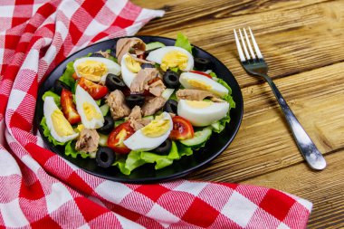 Marul, siyah zeytin, yumurta ve ahşap masada taze sebzeli lezzetli ton balığı salatası.