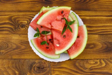 Tahta bir masanın üzerinde beyaz tabakta taze olgun dilimlenmiş karpuz. Üst görünüm