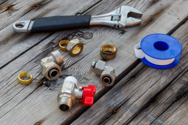 Çeşitli tesisat yedek parçaları, bant mühürleme ve ahşap arka planda ayarlanabilir ingiliz anahtarı.