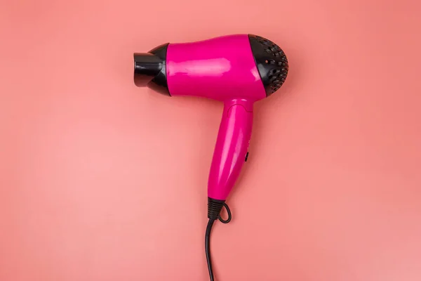 Pink hair dryer on a pastel pink background. Top view