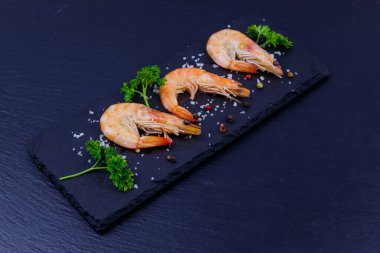 Siyah arkaplanda maydanozlu, tuzlu ve biberli büyük çiğ karidesler.