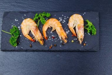 Siyah zemin üzerinde maydanozlu, tuzlu ve biberli büyük çiğ karidesler. Üst görünüm