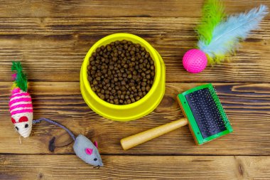 Kasede kuru kedi maması, kedi oyuncakları ve ahşap arka planda evcil hayvan fırçası. Üst Manzara. Hayvan bakımı konsepti