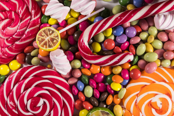 Background of colorful chocolate candies, lollipops, candy cane and marshmallows