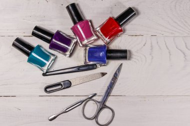 Beyaz ahşap arka planda temel manikür aletleri seti. Tırnak makası, tırnak makası, tırnak törpüsü ve oje şişeleri.