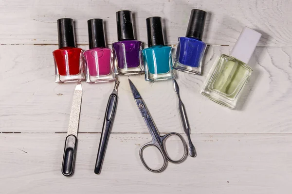 Basic set of manicure tools on white wooden background. Nail and cuticle scissors, cuticle trimmer, nail file and nail polish bottles on wood table