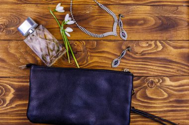Ahşap arka planda kadın aksesuarları. Debriyaj çantası, parfüm şişesi, kolye, küpeler ve tahta masada kar damlaları. Güzellik ve moda kompozisyonu. Üst manzara, düz uzanma