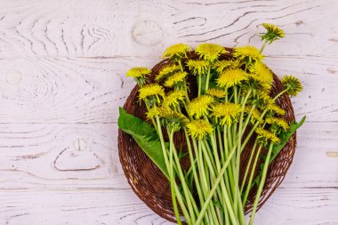 Hasır sepetteki sarı karahindiba çiçekleri beyaz ahşap arka planda. Üst görünüm