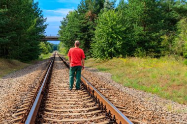 Yalnız adam tren yolunda yürüyor.
