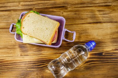 Sandviç ve ahşap bir masada bir şişe su ile beslenme çantası. Üst görünüm