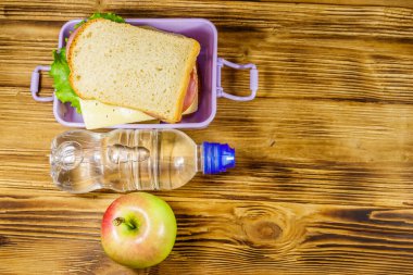 Sandviçli beslenme çantası, ahşap bir masada bir şişe su ve elma. Üst görünüm, alanı kopyala