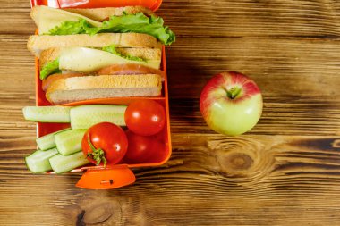 Elma ve beslenme çantası, sandviç ve taze sebzelerle ahşap bir masada. Üst görünüm