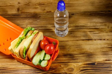 Bir şişe su, sandviç ve ahşap bir masada taze sebze.