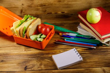 Okul konseptine geri dönelim. Okul malzemeleri, kitaplar, elma ve beslenme çantası içinde sandviçler ve ahşap bir masada taze sebzeler.