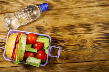 Bir şişe su ve hamburgerli beslenme çantası ve ahşap bir masada taze sebzeler. Üst görünüm, alanı kopyala